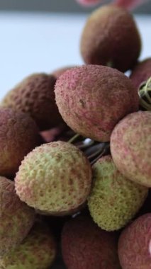 Bir dala asılmış liçi sürüsünün yakın çekimi, pürüzsüz pembe deri ve nemli ışıkta ince gövdeler. - Evet. Yüksek kalite fotoğraf