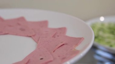 Bir tabak dilimlenmiş pembe et ürünü kırmızı bir yüzeyde duruyor, pürüzsüz dokusunu ve kendine özgü şeklini sergiliyor. Yüksek kalite fotoğraf