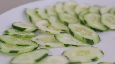 Kesilmiş salatalıkların üst yakın çekimi, güçlü bir yansıma arka planına sahip, siyah tabakta dönüyor..