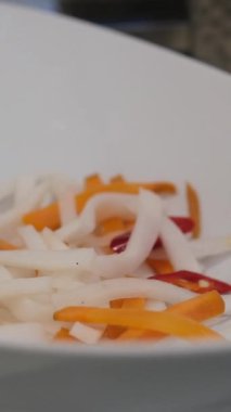 Soyulmuş taze havuç ve daikon turpu dilimleri, soyulmamış daikon turplarının yarısı beyaz bir masada yatıyor. Havuç, Daikon turpu, sebze salatası ve abur cuburlarda popüler malzemeler.