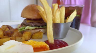 Lezzetli bir Burgerle Patates Yiyen Adam. Patates kızartması ketçapa batırılmış.