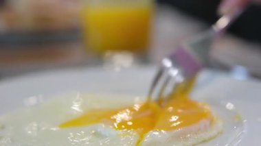 Omleti kesen çatal ve bıçağın yakın çekimi ve tabakta güneşli yumurtalar. portakal suyu, mango suyu öğle yemeği.