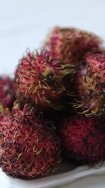 Dikey ekran Rambutanların yakın çekimini gösteriyor, egzotik dikenli meyveler, bir sepetin içinde üst üste yığılmış. meyvelerin eşsiz, kıllı bir dokusu ve tropikal bölgelerde popüler olan parlak kırmızı ve yeşil renkleri vardır..