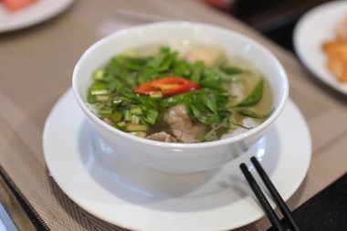 Beyaz tabakta fesleğen ve kırmızı biberli Vietnamlı pho bo bo