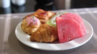 Beyaz bir tabakta karpuz parçaları ve açık büfedeki diğer tatlılar.