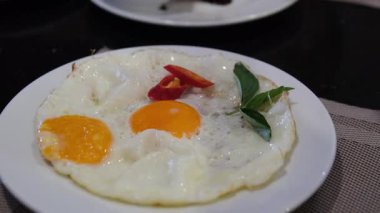 Fesleğenli sahanda yumurta ve kırmızı biber beyaz tabağa kızarmış domuz pastırması ekle.