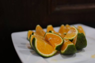 portakal dilimleri yeşil Vietnam portakalları turunçgiller bir dalda asılı, parlak yapraklarla çevrili. Açık havada doğal ışık altında, canlı ve taze detayları vurguluyor.