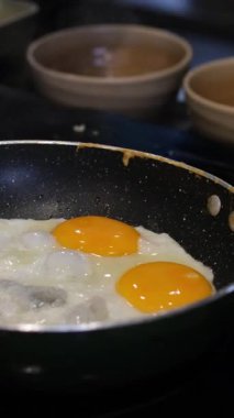 Fırında yumurta pişiren el, bir yumurtayı fırının tepsisine kırıyor. Bu yakın çekim yemek pişirmenin ilk aşamalarını ve basit bir yemeğin hazırlanmasını yakalar.