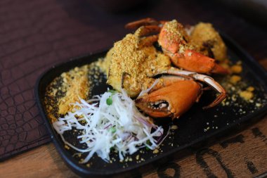 Masaya renkli bir yengeç kızartması koyan, zengin dokusunu ve süslerini sergileyen ellerin yakın çekimi. Yüksek kalite 4k görüntü