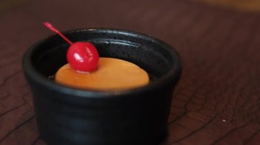 Bir el, beyaz bir tabağı dolduran karamelize edilmiş büyük bir pudingin üstüne kiraz koyar. 4K ağır çekim. Yüksek kalite 4k görüntü
