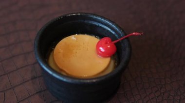 Bir el, beyaz bir tabağı dolduran karamelize edilmiş büyük bir pudingin üstüne kiraz koyar. 4K ağır çekim. Yüksek kalite 4k görüntü