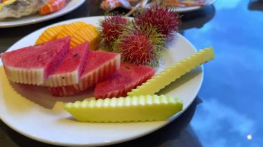 Bir tabak mango papaya frambutan karpuz üzerine açık büfe ve yakınlardaki deniz ürünleri masa yengeçleri karides langoustine istiridyeleri. Yüksek kalite 4k görüntü