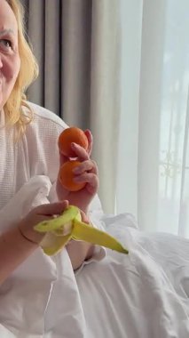 Kadın yatakta muz ve mandalina yiyor. Meyve yiyen bir kadın. Yüksek kalite 4k görüntü