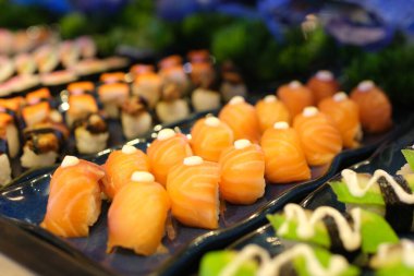 Gourmet somon suşi ruloları siyah bir tabakta garnitürlerle servis edilir, güzel bir yemek deneyimi için hazırdır. Yüksek kalite