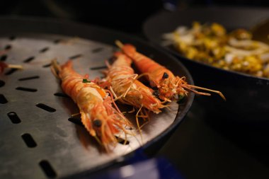 Şef karidesleri ızgarada pişirecek, her biri yemek pişirme yeteneğinin göstergesidir. Izgaranın sihrine şahit olun. Karidese dumanlı bir tat veriyor. Izgaranın kokusuna kapıl..