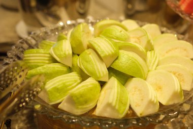 Guava, guava tabağını tam bir guava tabağıyla dilimliyor ve ortada düzgünce düzenlenmiş dilimlenmiş parçalarla çevrelenmiş yapraklar var.
