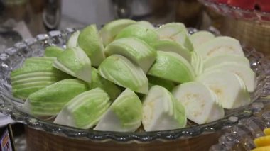 Guava, guava tabağını tam bir guava tabağıyla dilimliyor ve ortada düzgünce düzenlenmiş dilimlenmiş parçalarla çevrelenmiş yapraklar var.