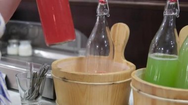 Süpermarket raf ortamında gerçekleşen bir şişe seçiminde karpuz suyu, müşteri eli birden fazla içecek seçeneği arasında parlak cam kaplara doğru uzanıyor. Yüksek kalite 4k 