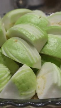 Guava, guava tabağını tam bir guava tabağıyla dilimliyor ve ortada düzgünce düzenlenmiş dilimlenmiş parçalarla çevrelenmiş yapraklar var.