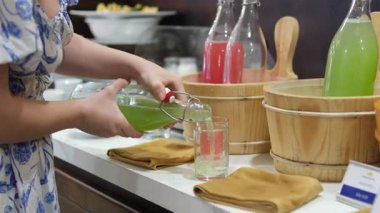 Masanın üzerinde çeşitli içecekler var. Ahşap küvetler, karpuz, yeşil kereviz ve salatalık dişilerin elleri bardağa detoks döküyor. Yüksek kalite 4k görüntü