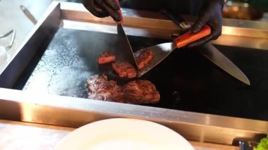 Şef biftek pişiriyor, arka planda profesyonel mutfağa tuz serpiştiriyor, ağır çekimde. Yüksek kalite 4k görüntü