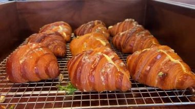 Altın rengi kruvasanlar ahşap tahtalarda, çörek ve pasta dilimleri gibi diğer hamur işlerinin yanında muhtemelen kahvaltı büfesinde ya da fırında sergileniyor. Yüksek kalite 4k görüntü