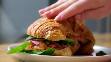 Kruvasan sandviçi, yanında Serrano jambonu ve roka yaprakları. Ellerini kruvasanın üstüne koy, sağlıklı yiyecekler. Yüksek kalite 4k görüntü
