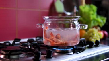 Evde karides haşlama. Yakından bakınca, bir kadın eli fırının tepesinde körfez yaprakları ve biberlerle kaynayan bir karides tenceresini karıştırıyor. Yüksek kalite 4k görüntü