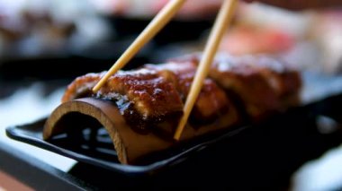 Farklı rulo, nigiri, maki, gunkan içeren düz bir tabakta süslü siyah suşi. Japon ulusal mutfağı yakın plan. Yemek çubukları füme yılan balığı.