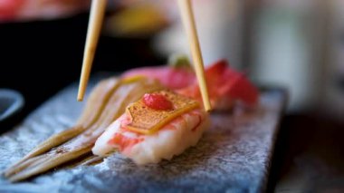 Kamera yukarı taşır. Şık koydu suşi soya sosu ve Çin bambu sopalarla yanındaki siyah ahşap arka plan olarak ayarla. Somon balığı, yılanbalığı, salatalık karides ve diğer çeşitli doldurma ile çeşitli suşi rulo.