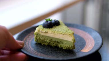 Yeşil kek dilimi, kirazlı yaban mersini, bir dilim peynirli kek ahşap masada gösteriliyor. Dilimler ikiye bölünmüş ve bir bıçakla tutuluyor. Hoşgörü ve zevk kavramı. Yüksek kalite