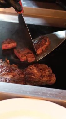 Şef biftek pişiriyor, arka planda profesyonel mutfağa tuz serpiştiriyor, ağır çekimde. Yüksek kalite 4k görüntü