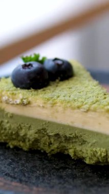 Yeşil kek dilimi, kirazlı yaban mersini, bir dilim peynirli kek ahşap masada gösteriliyor. Dilimler ikiye bölünmüş ve bir bıçakla tutuluyor. Hoşgörü ve zevk kavramı. Yüksek kalite