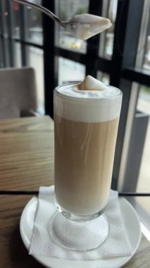 İçi sıcak kahve dolu, köpüklü, kalın bir kahve fincanı ve içinde kahve aşıkları için mükemmel bir kaşık olan bir kaşık. Köpüğü temizlemek için çay kaşığı kullan.