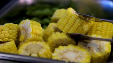 İki pişmiş biftek ve göl kıyısında dört mısır koçanı tezgahı olan barbekü brazier. Aşçı mısır koçanlarını mutfak maşasıyla çevirir. Yüksek kalite 4k görüntü