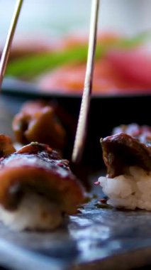 Yemek çubukları Japon restoranında Japon suşisi yer. Geleneksel suşi Maki Rolls with Tuna Philadelphia Cheese Avocado, Salatalık, Rice and Nori. Japon Suşi Roll Uramaki, Nigiri ve Hosomaki.