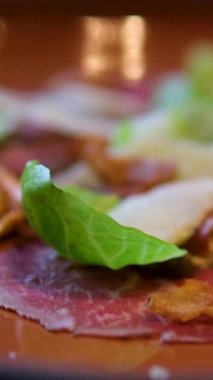  Fransız restoranında siyah arka planda, siyah bir tabakta parmesan peynirli, marullu, kaprisli, siyah zeytinli ve pesto soslu leziz geleneksel sığır etli carpaccio. Yüksek kalite 4k