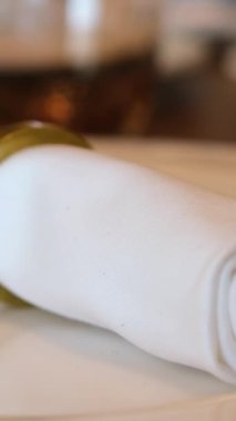 Lüks altın Noel sofrası. Parlak masa örtüsü, cam tabakta çelik peçete halkası, çatal bıçak takımı, şamdanlar. Arka planda aydınlatan Xmas ağacı. Şenlikli yeni 