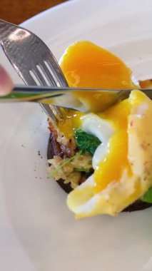 Benedict yumurtalı, salatalı, meyveli ve portakallı sağlıklı kahvaltı yapan kişi açık kafede. Taze, besleyici sabah yemeği konsepti. Ağır çekim. Yüksek kalite 4k görüntü