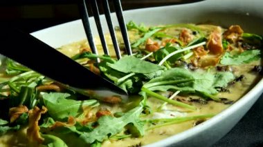 roka güveç salatası, vişneli domates ve beyaz tabakta pesto soslu burrata. Kadınların elleri yumuşak peyniri çatal ve bıçakla keser. Yakın plan, yan görüş. Yüksek kalite