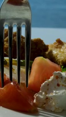 Roka salatası, vişneli domates ve kafede beyaz bir tabakta pesto soslu burrata. Bir kadının eli, yumuşak peyniri çatal ve bıçakla keser. Yakın plan, yan görüş. Yüksek kalite 4k görüntü