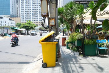 Sarı çöp tenekesi gökdelenlerin yanında motosiklet ağaçları Vietnam Ho Chi Minh Şehri 08.04.2025
