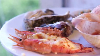 Kırmızı biber soslu çıtır badem kabuklu karidesler, yenilebilir çiçekler ve mikroyeşilliklerle süslenmiş, mavi seramik bir tabakta servis ediliyor. Canlı deniz ürünleri tabağı. 