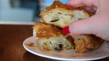 Tırnakları boyalı ve akıllı bir insan açık bir kafede beyaz bir tabakta çikolatalı kruvasan kırar. Yüksek kalite 4k görüntü