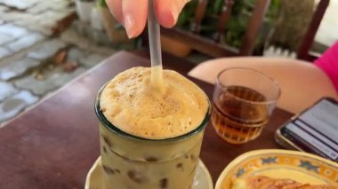 Buzlu buzlu kahveyi, deniz kenarında sıcak bir günde su damlacıklarıyla kaplı bir bardakla karıştırmak. Yüksek kalite 4k görüntü