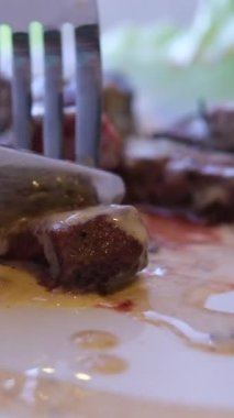 Beyaz, kavrulmuş bir yüzey kenarındaki ızgara bifteği kesen bir çatal ve bıçağın yakın plan çekimi ve sulu doku bifteğin zengin lezzetini ve hassasiyetini ön plana çıkarıyor. Yüksek kalite 4k görüntü