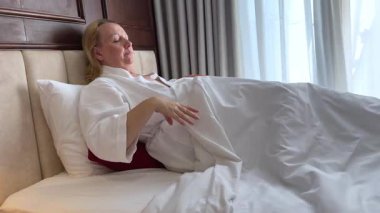 Sabah uyandığında battaniyenin altında uzanmış orta yaşlı bir kadın uykusuna döner ve sağ tarafta kırmızı yastığa sarılır. Yüksek kalite 4k görüntü