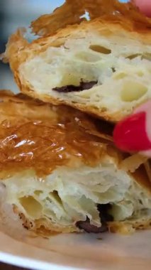 Tırnakları boyalı ve akıllı bir insan açık bir kafede beyaz bir tabakta çikolatalı kruvasan kırar. Yüksek kalite 4k görüntü