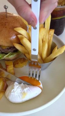 Tabağa çatal ve bıçakla yumurta kesip Fast Food kızartması ve kafede et köftesi yiyen bir kız. Yüksek kalite 4k görüntü