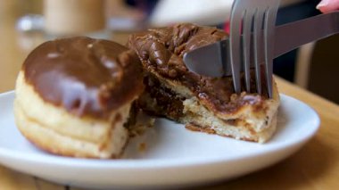 Dilimlenmiş bir Berlinli çörek sergilenirken, kremalı çikolata dolgusu ve yumuşak hamuru ortaya çıkıyor. Parlak çikolata jölesi beyaz çikolata parçacıklarıyla kaplıdır..